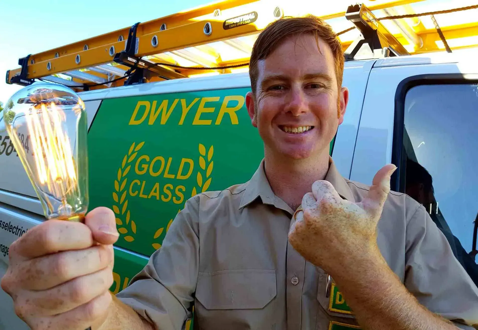 A man is holding a light bulb in front of a dwyer gold class van
