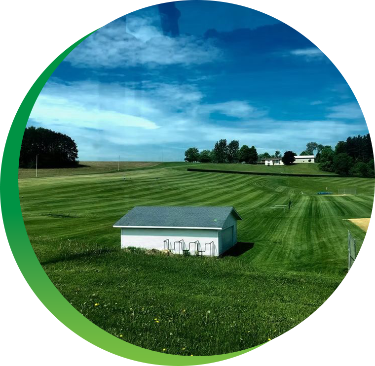 A small white house sits in the middle of a lush green field