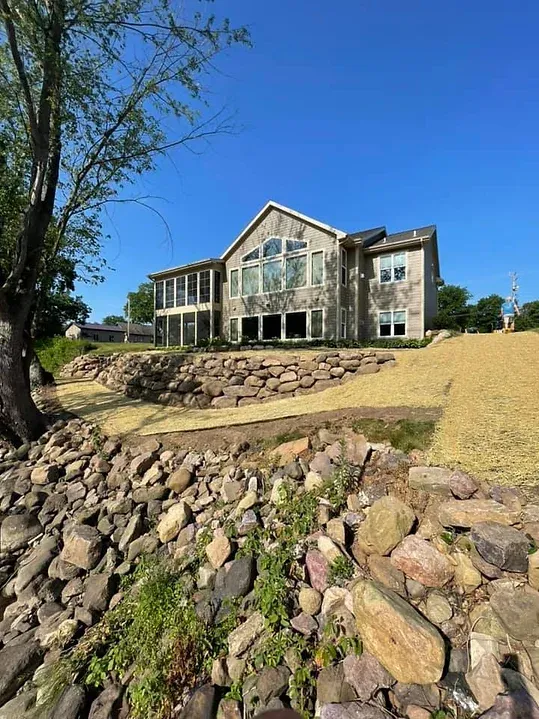 A large house is sitting on top of a hill next to a rock wall.