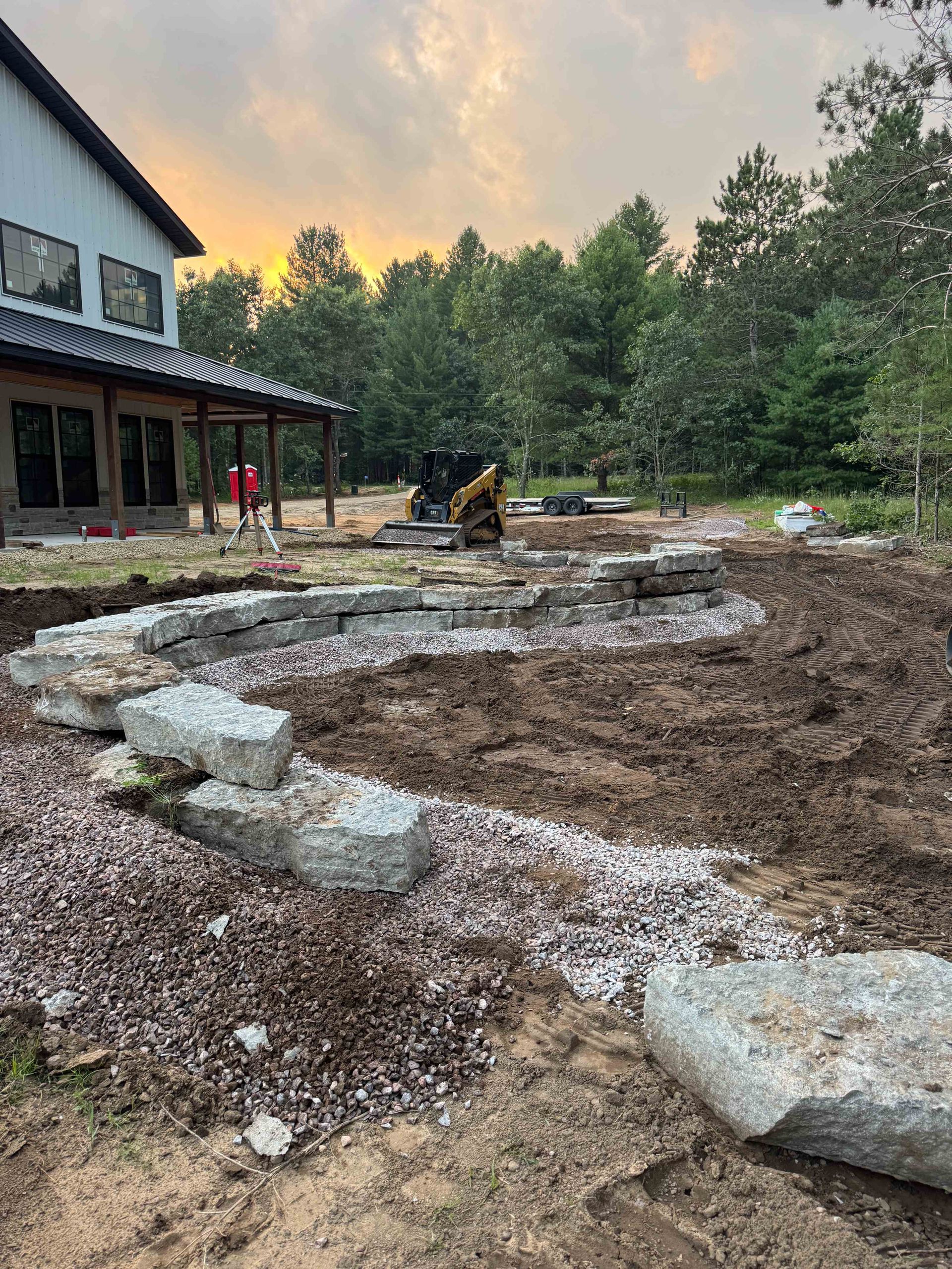 Large granite stone blocks forming a curved retaining wall in a yard under construction near a modern house.