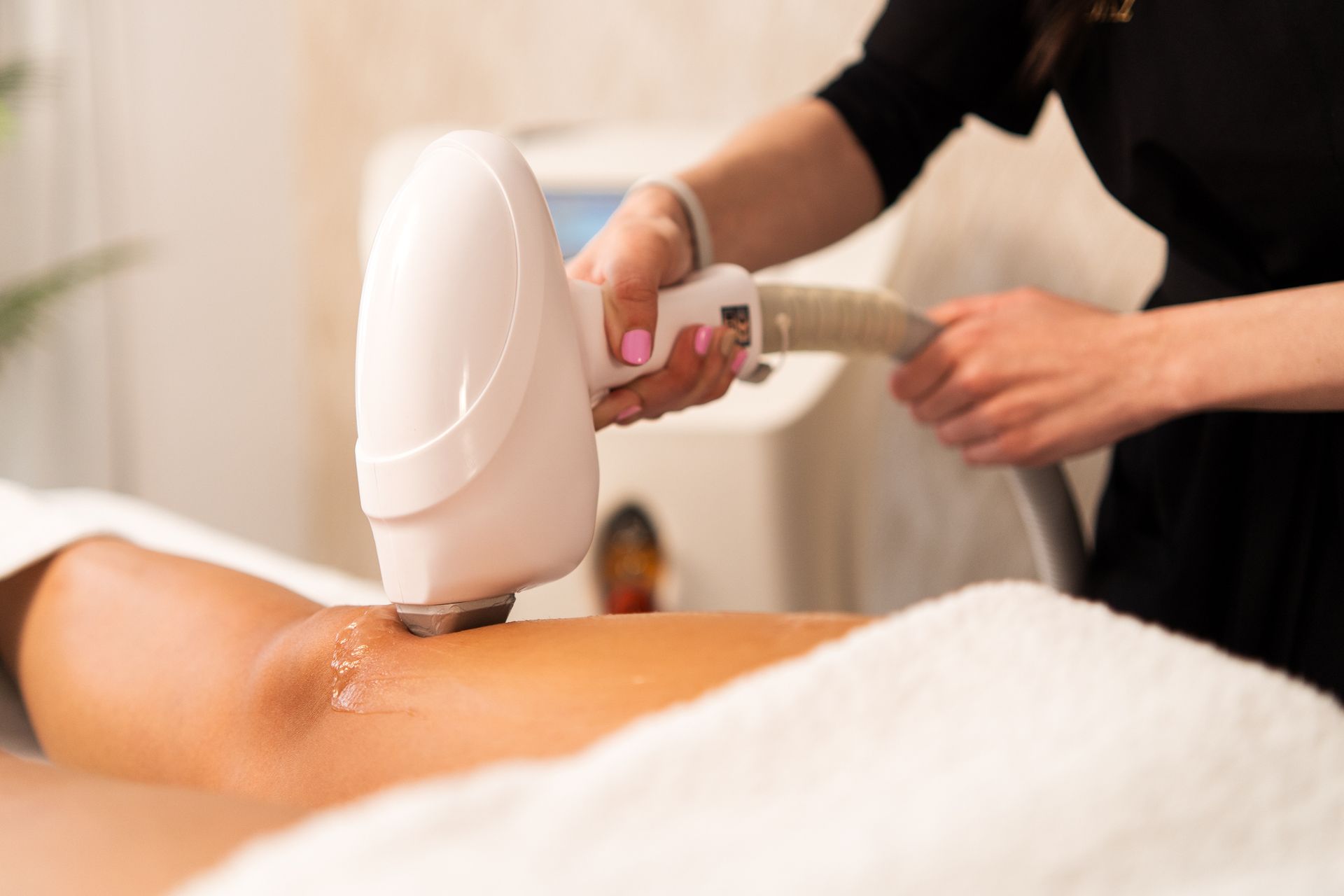 Una persona che utilizza un dispositivo laser per la depilazione su una gamba, con un asciugamano bianco e un apparecchio sullo sfondo.