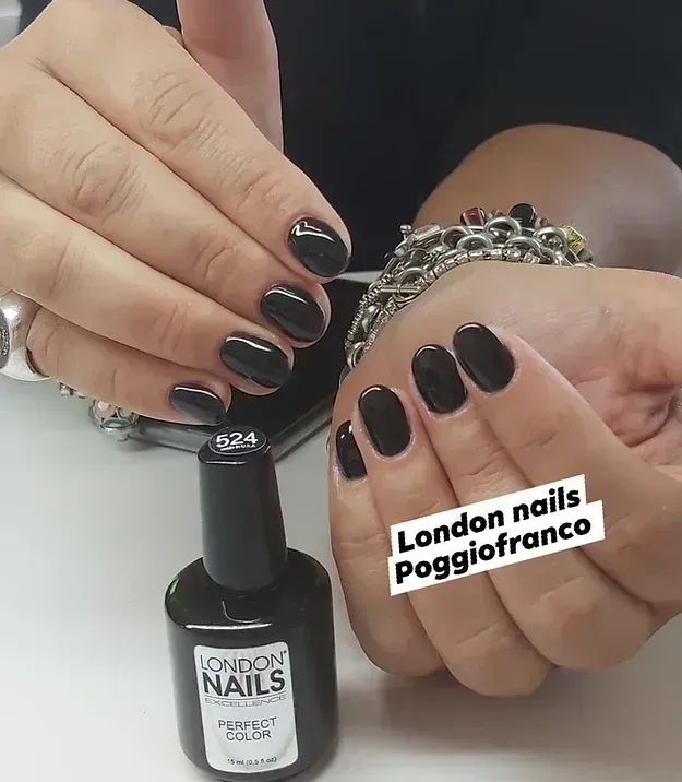 Mani con manicure in gel nero, che tengono in mano una boccetta di smalto. Etichetta