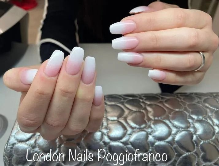 Mani di donna con unghie quadrate sfumate dal bianco al rosa; appoggiate su una superficie argentata.