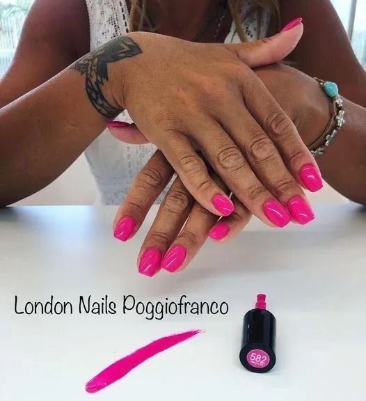 Mani di donna con smalto rosa acceso, incrociate su una superficie bianca. Accanto, boccetta di smalto e campione.