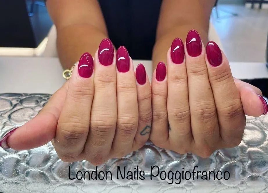 Mani con unghie a mandorla dipinte di un intenso color bordeaux, in posa per la pubblicità di un salone di bellezza.