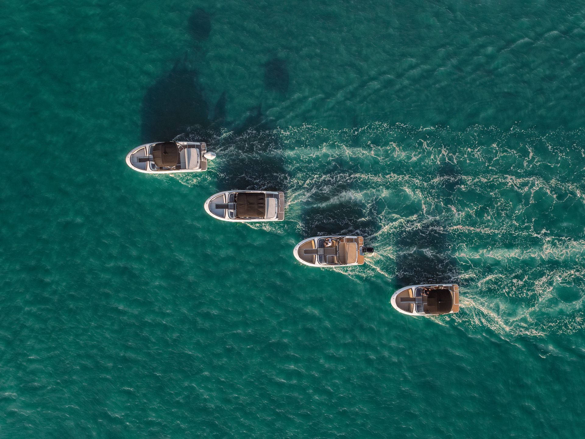Four boats moving on teal water, leaving white wakes.