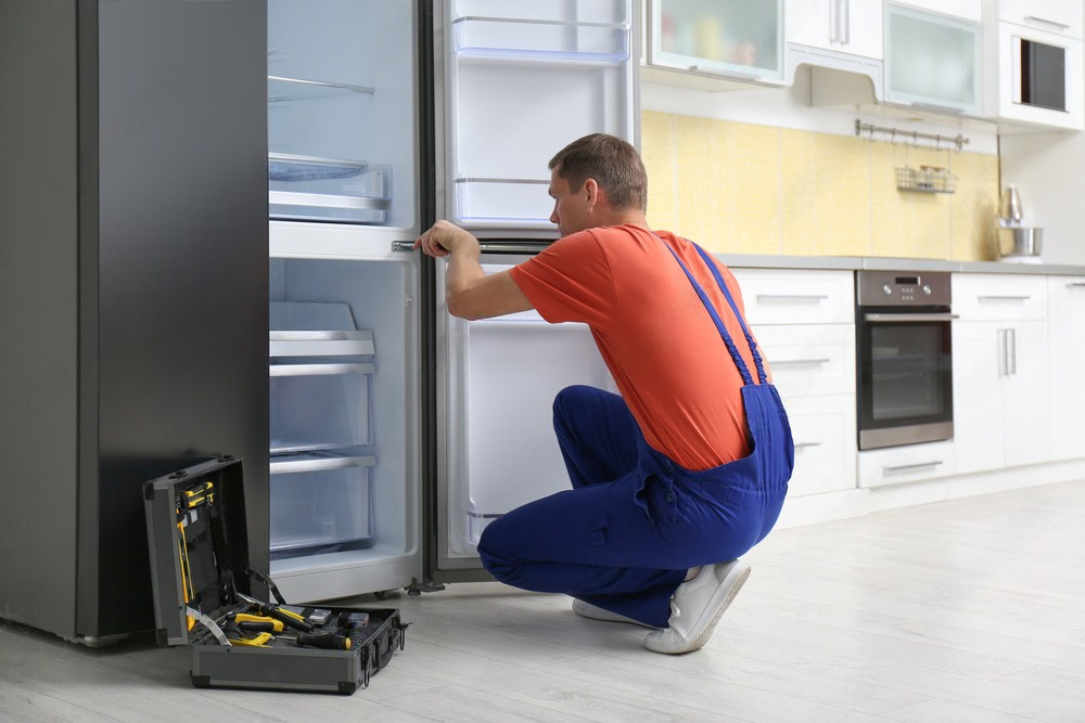 a man is repairing a refrigerator in a kitchen .