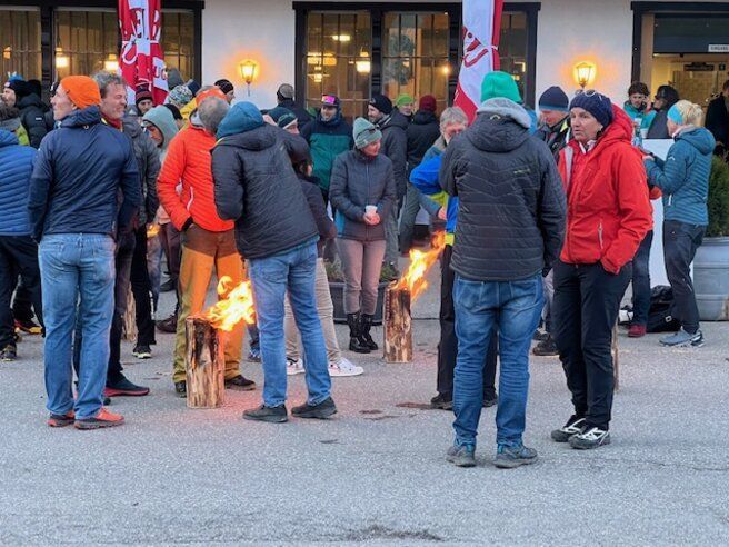 Eine Gruppe von Menschen steht vor einem Gebäude um ein Feuer herum.