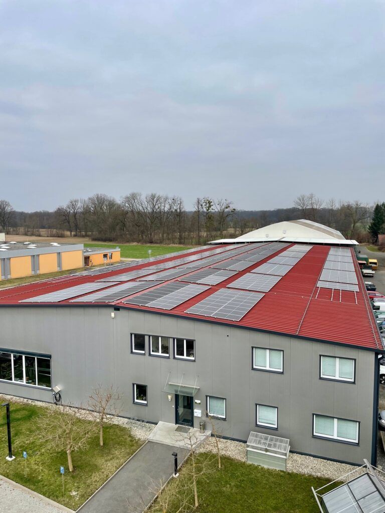 Großes Industriegebäude mit Solarpaneelen auf dem Dach, unter bewölktem Himmel.