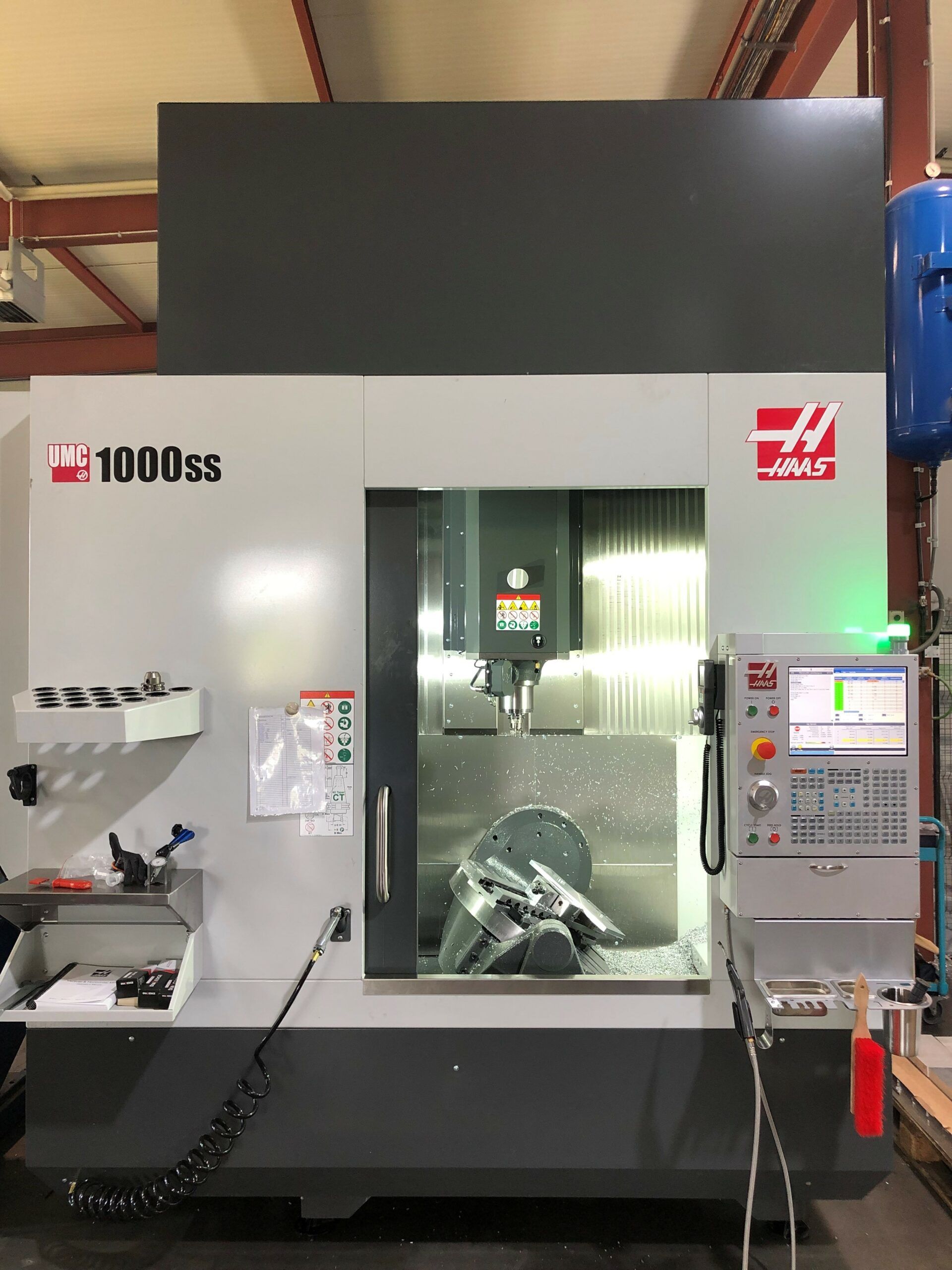 Graue Haas VF-1000ss CNC-Fräsmaschine in einer Werkstatt, die Metall bearbeitet, wobei sichtbare Späne entstehen.