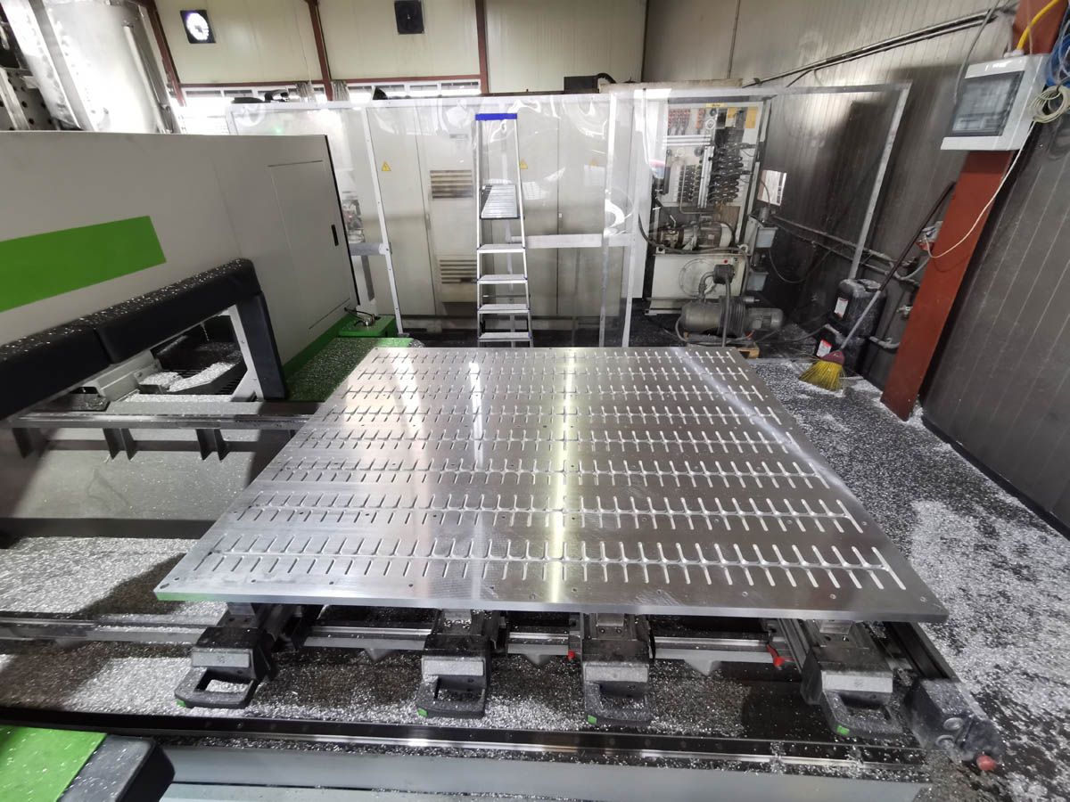 Große industrielle CNC-Maschine mit einem mit Löchern und Schlitzen versehenen Metalltisch in einer Werkstattumgebung.