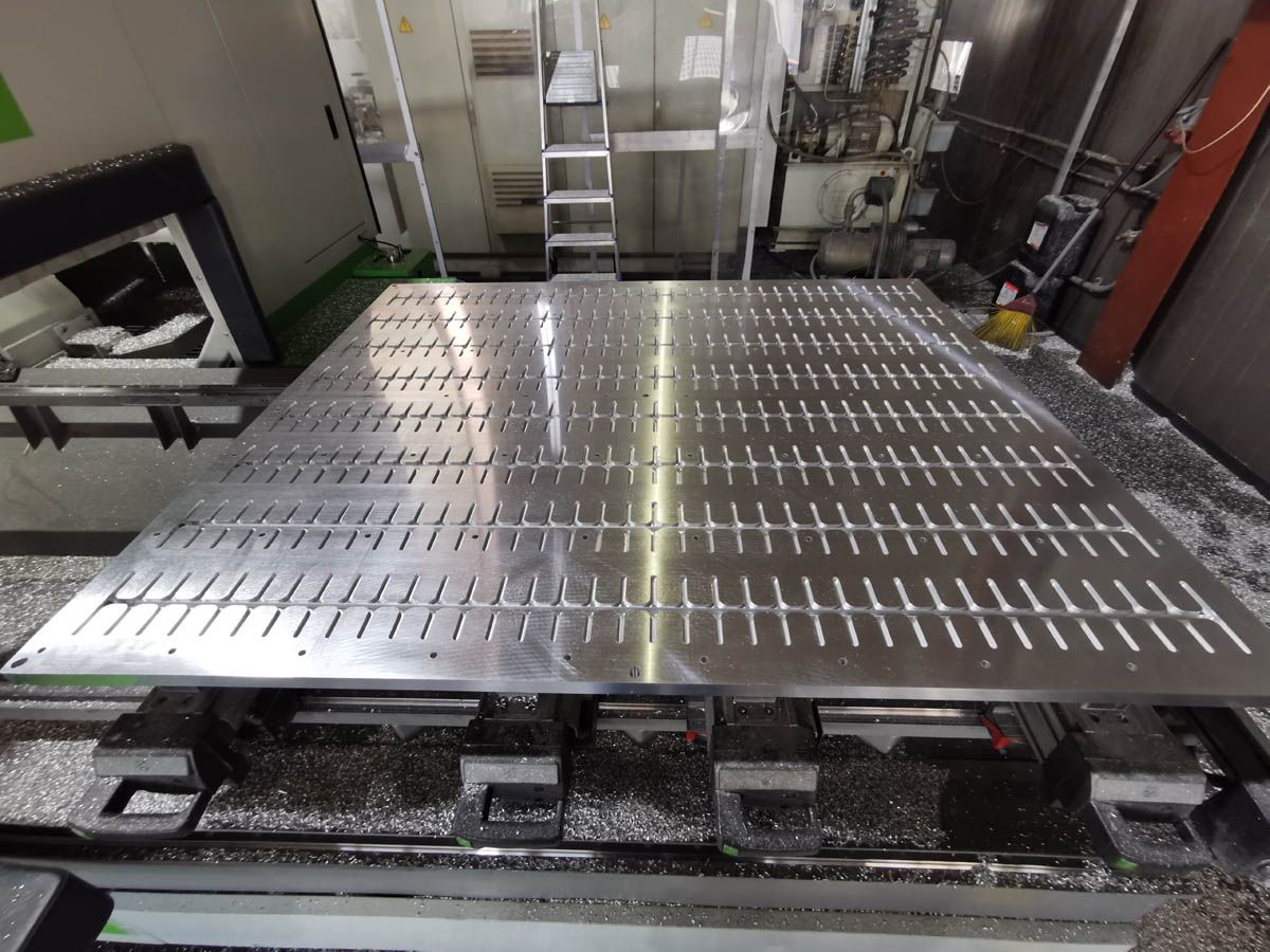 Ein großer Metalltisch mit vielen vertikalen Schlitzen in einer Produktionsumgebung, bedeckt mit Metallspänen.