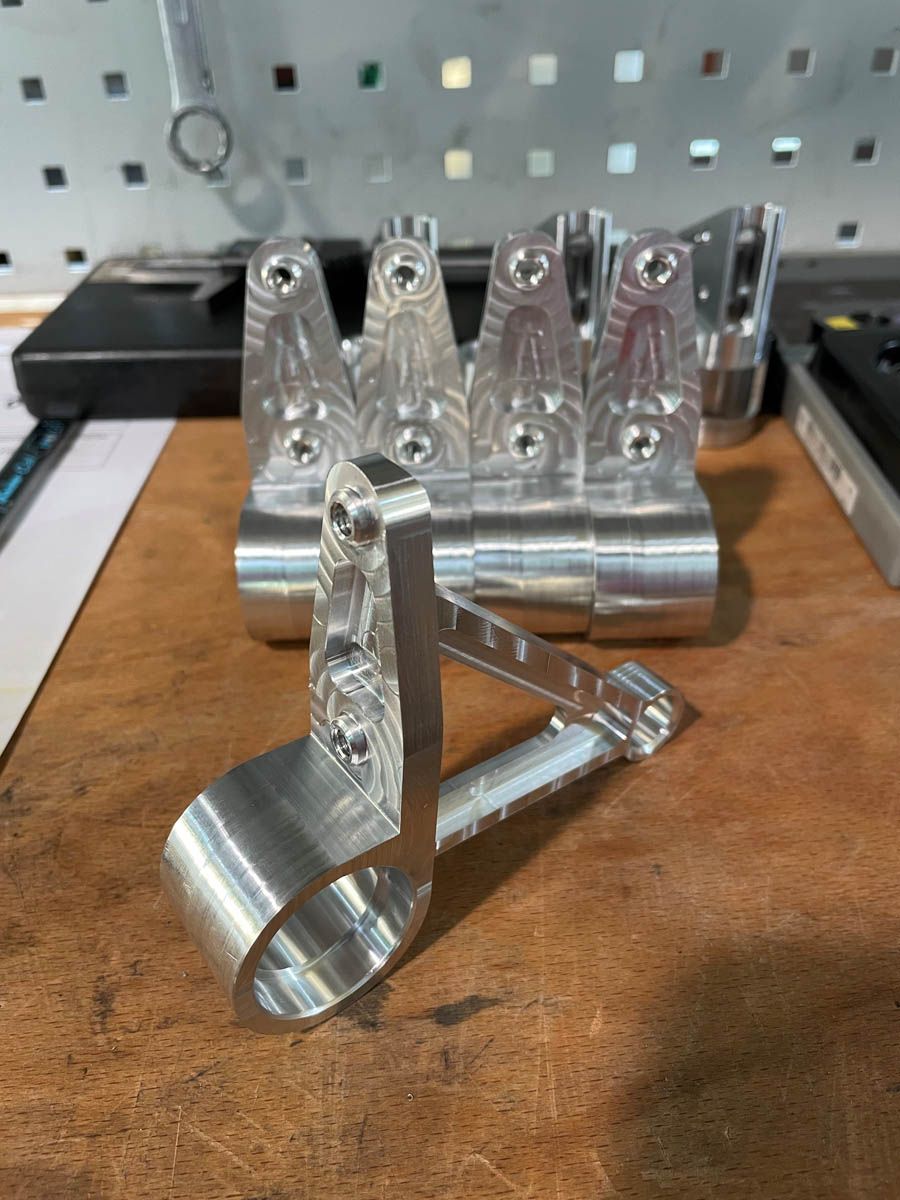 Mehrere bearbeitete Aluminiumhalterungen auf einer Werkbank, mit gebohrten Löchern und einem gebogenen Klemmbereich.