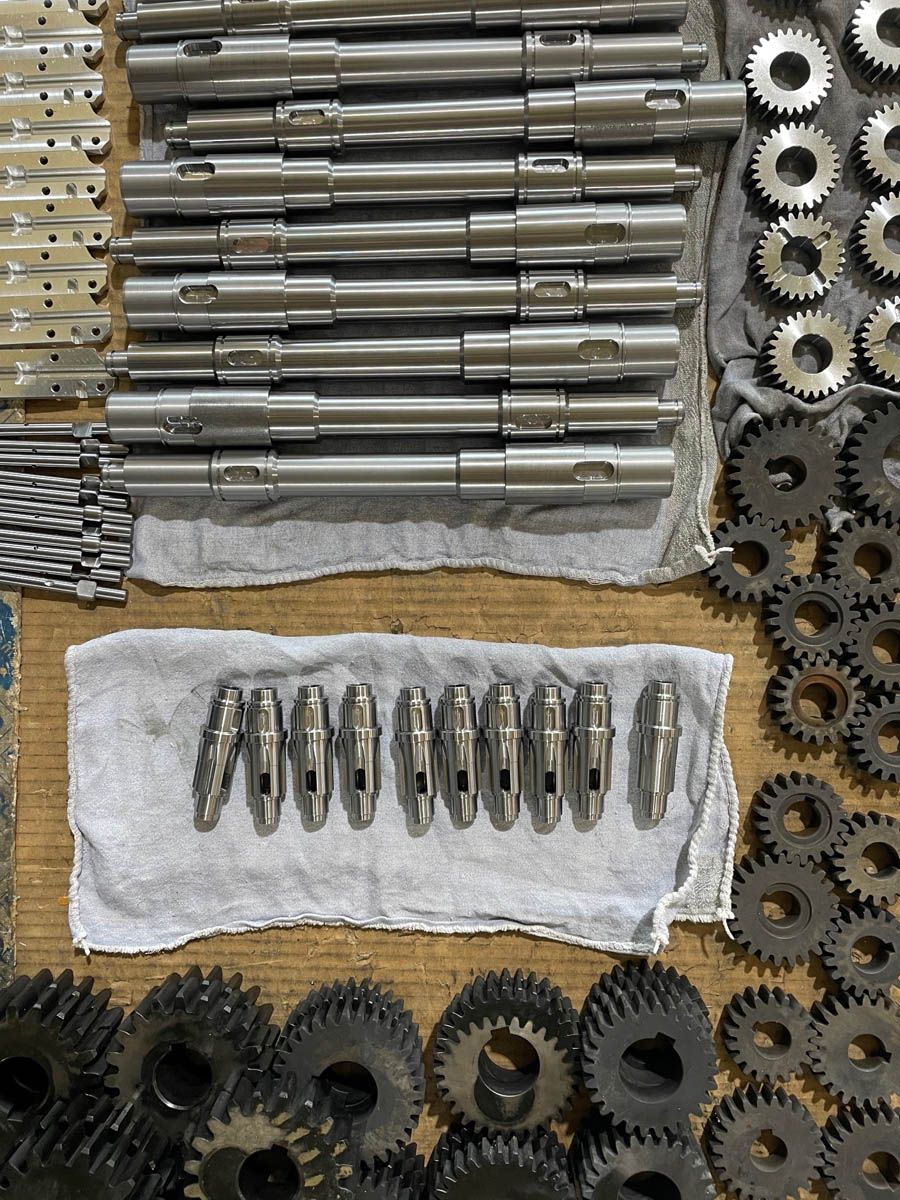 Metallische Maschinenteile, einschließlich Wellen, Zahnräder und Stifte, die auf einer Oberfläche angeordnet sind.