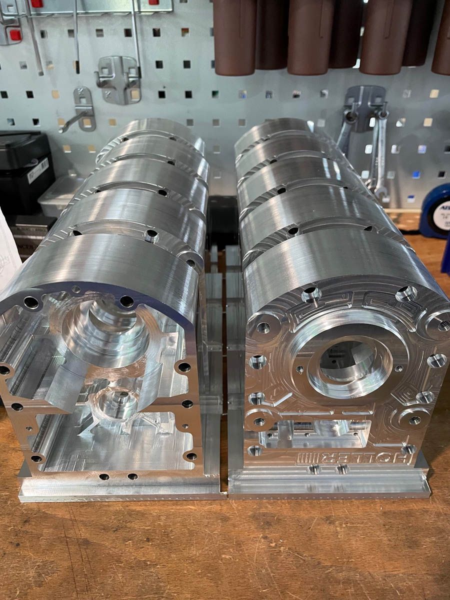Zwei bearbeitete Aluminiumteile mit aufwendigen Details, möglicherweise Motorkomponenten, auf einer Werkbank.