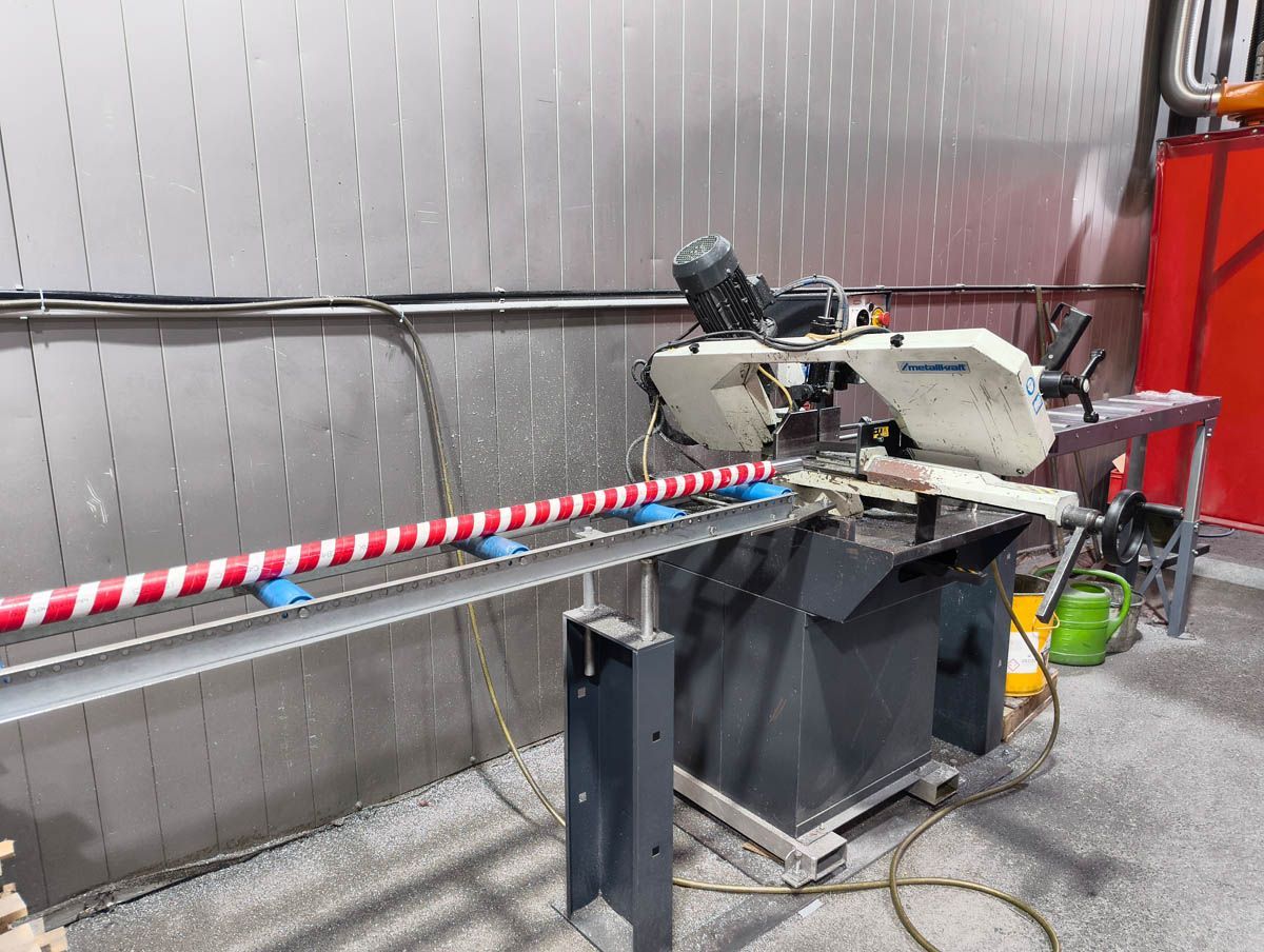 Bandsäge schneidet ein rot-weiß gestreiftes Rohr, industrielle Umgebung.