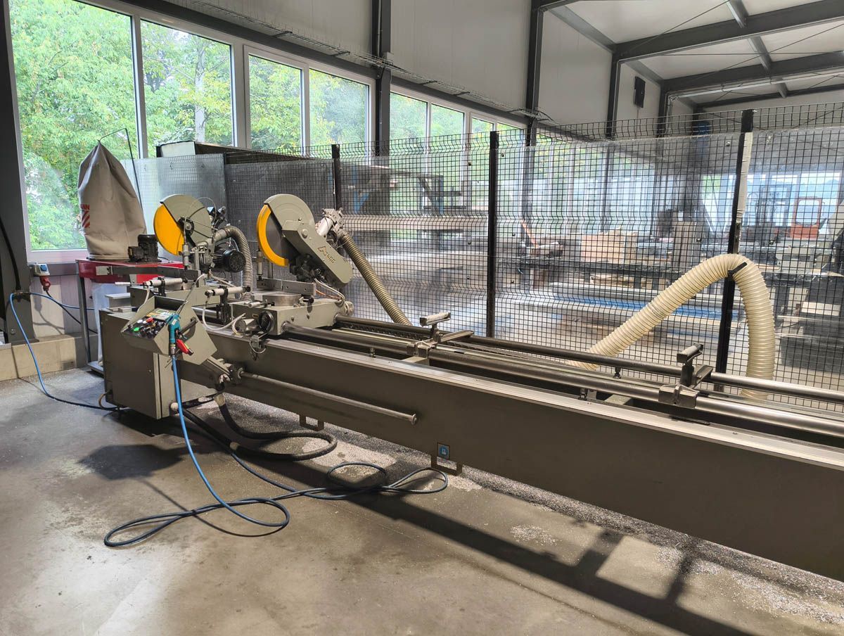 Metallschneidmaschine in einer Werkstatt. Grau, mit langer Führungsschiene und Sägeblättern.