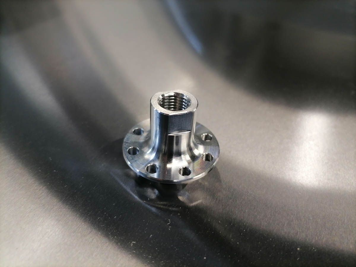 Flanschmutter aus Edelstahl auf einer metallischen Oberfläche, mit Sechskantkopf und mehreren Befestigungslöchern.