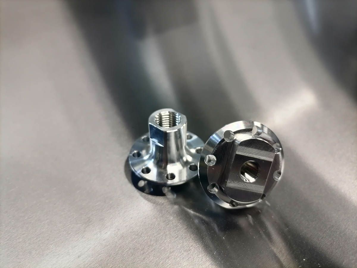 Zwei glänzende mechanische Metallteile auf einer reflektierenden silbernen Oberfläche.