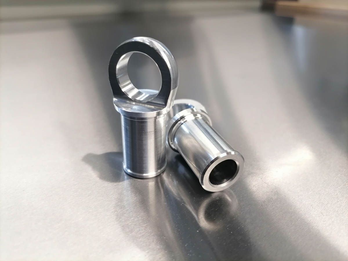 Zwei silberne Metallschleifenanschlüsse auf einer reflektierenden Oberfläche, einer aufrecht, der andere seitlich liegend.