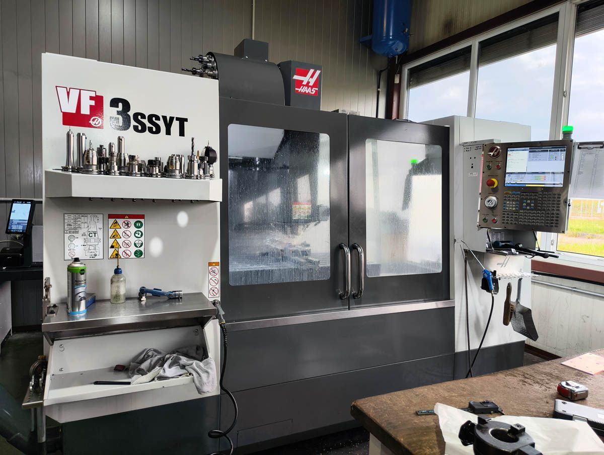HAAS VF-3SSYT CNC-Fräsmaschine in einer Werkstattumgebung, mit Metallbauteilen und Werkzeugen in der Nähe.