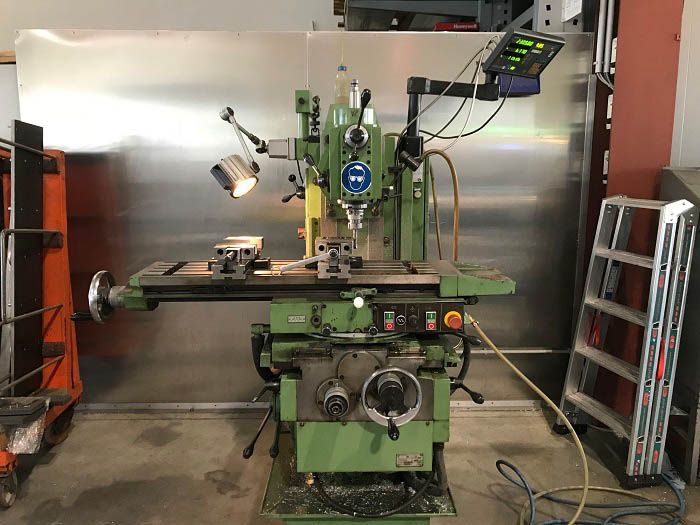 Grüne Fräsmaschine in einer Werkstatt, mit einem auf dem Tisch eingespannten Werkstück.