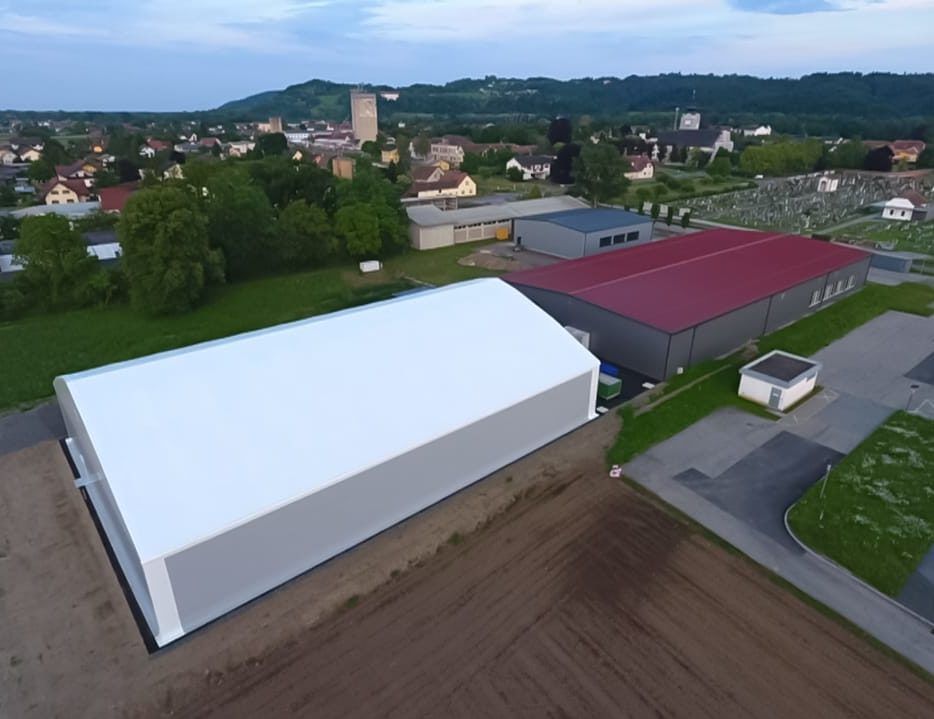 Luftaufnahme von Industriegebäuden mit weißen und roten Dächern, im Hintergrund die Stadt.