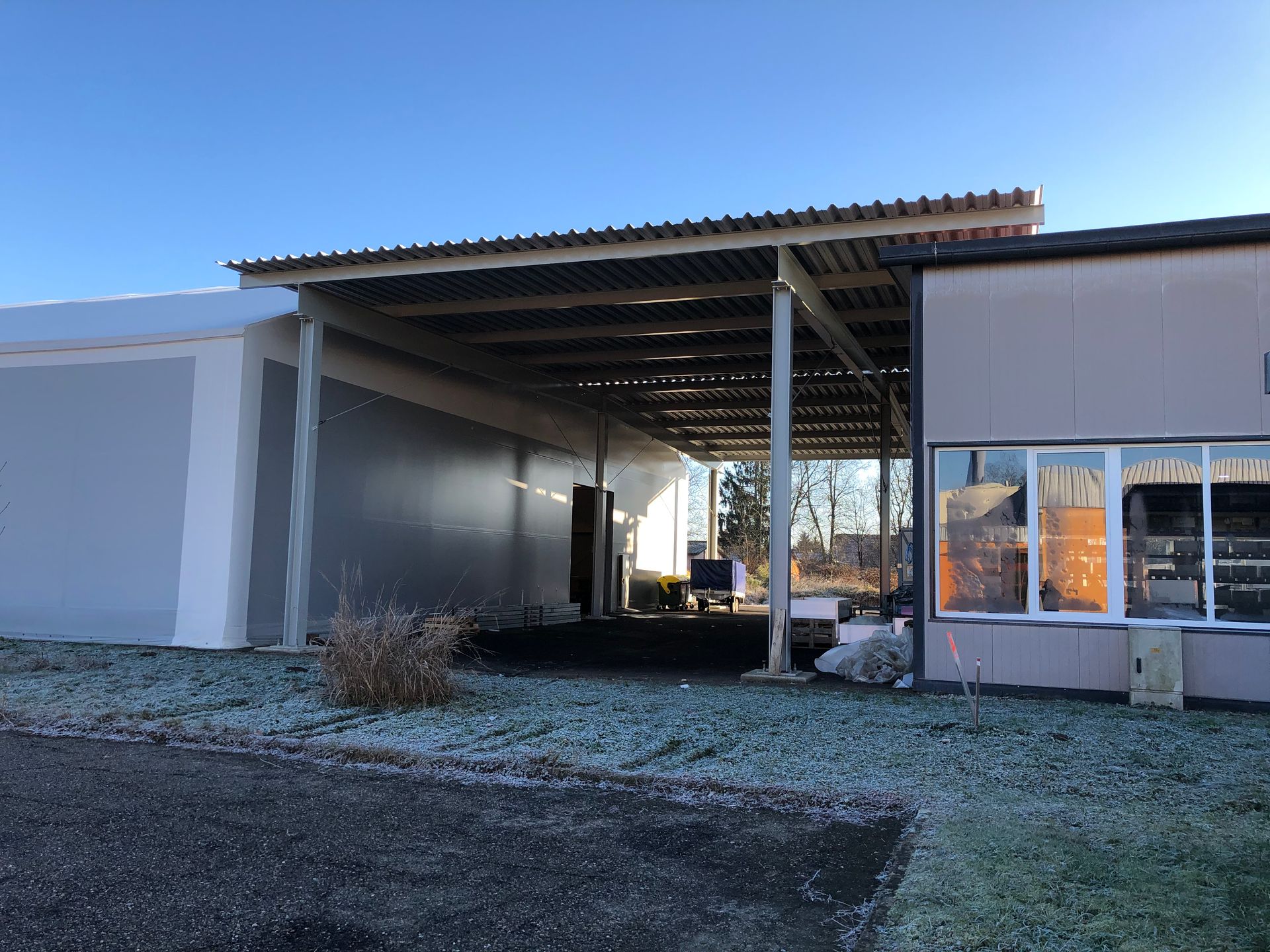 Überdachter Außeneingang eines Gebäudes mit Metalldach. Winterszene mit vereistem Boden und hellem Himmel.