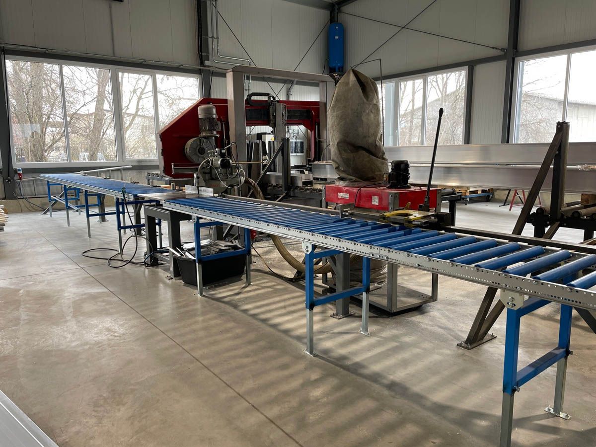 Industriesäge mit Förderband in einer Werkstatt.
