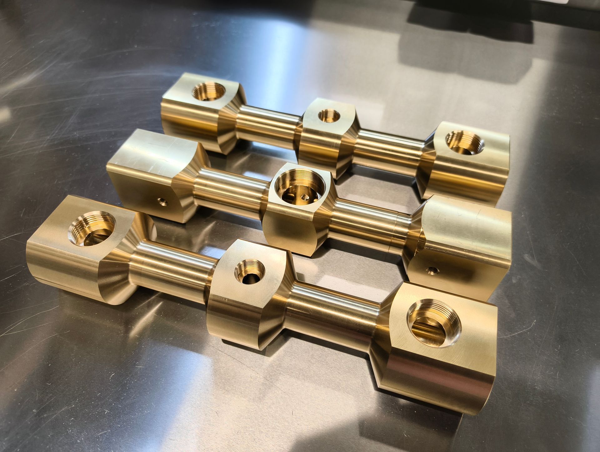 Drei Verbindungsstangen aus Messing auf einer Metalloberfläche.