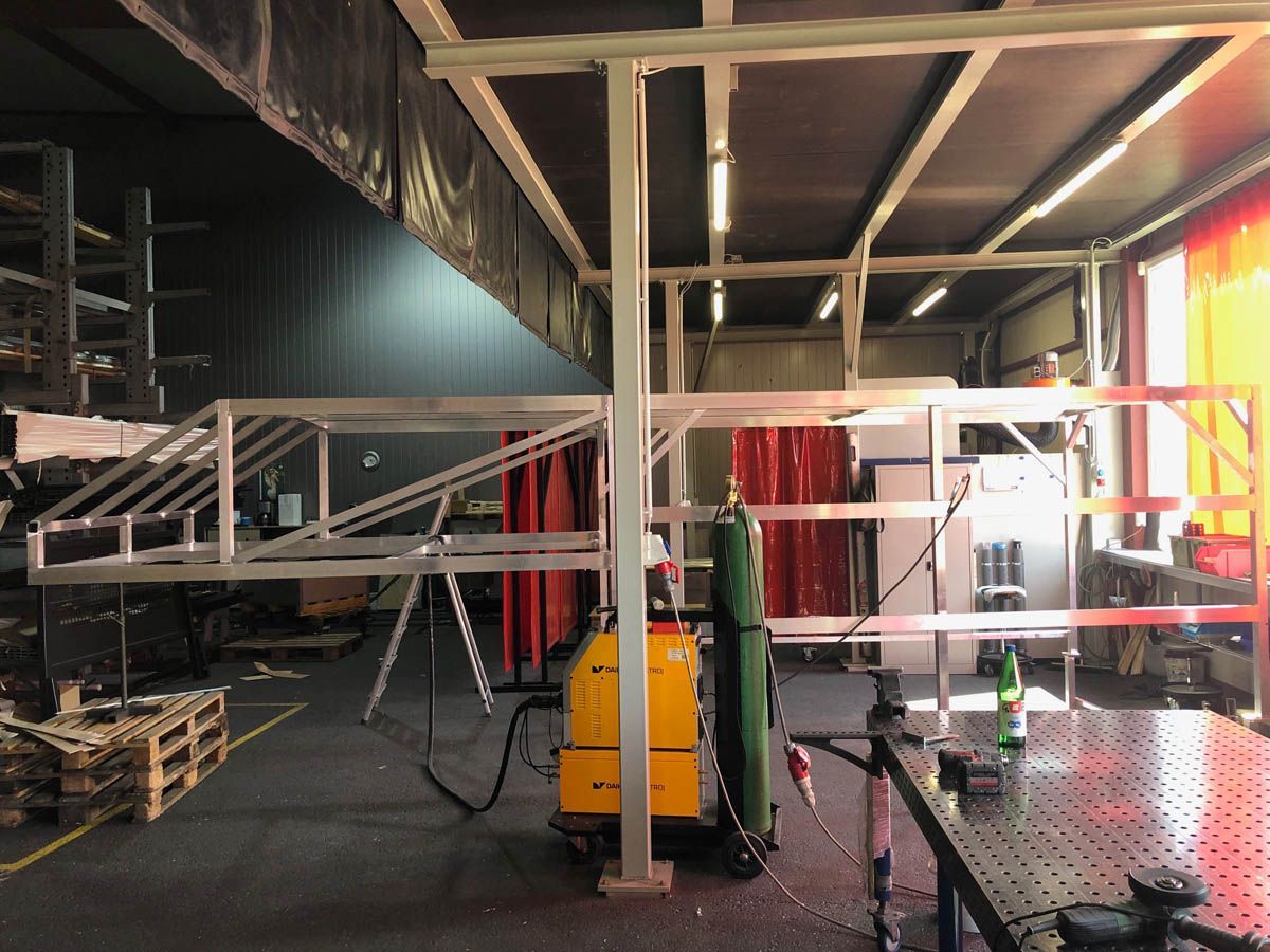 Schweißwerkstatt: Metallrahmenkonstruktion mit Schweißgerät und rotem Sicherheitsvorhang.