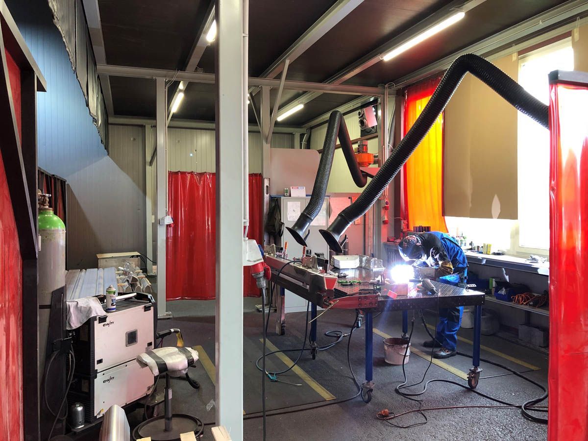 Ein Schweißer in blauem Overall schweißt Metall an einem Arbeitsplatz in einer Werkstatt