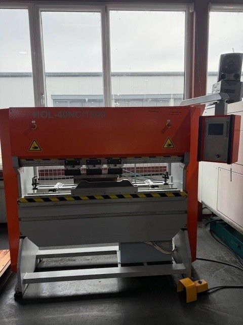 Orange und graue Metallbiegemaschine mit Bedienfeld und Fußpedal in einer Fabrikumgebung.