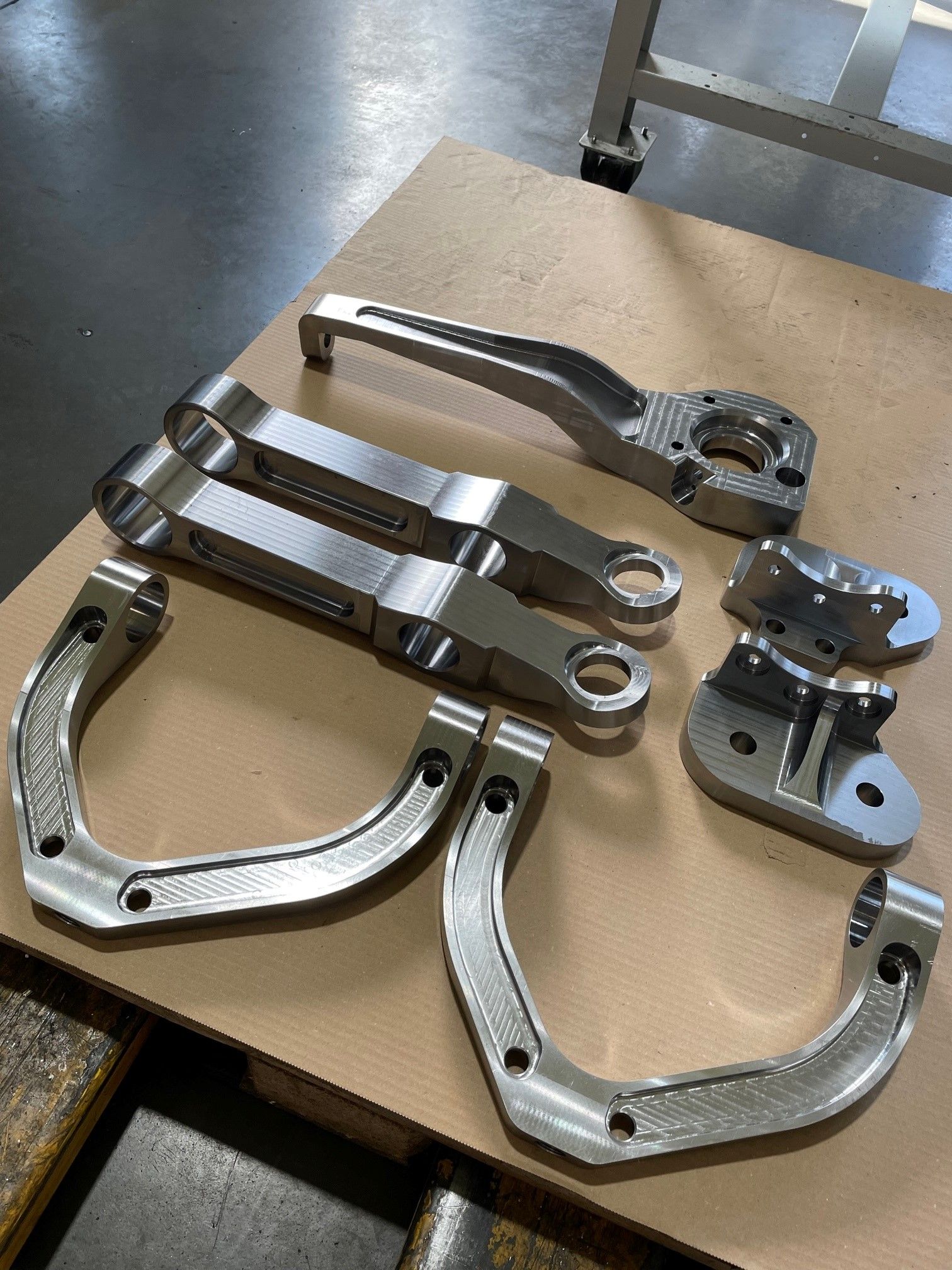Bearbeitete Aluminiumteile, darunter Hebel und Halterungen, sind auf einer Holzoberfläche angeordnet.
