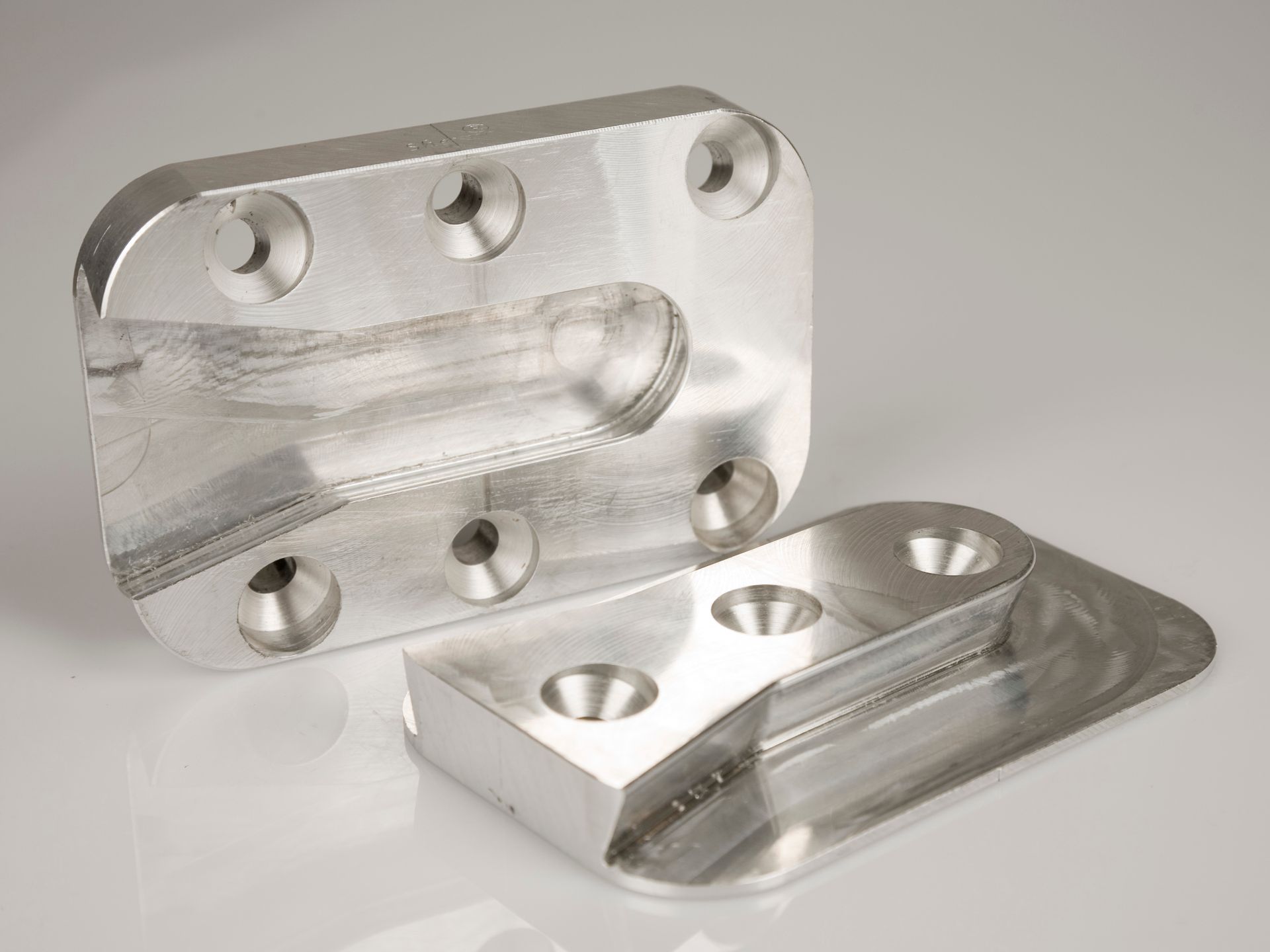 Zwei silberfarbene, maschinell bearbeitete Metallteile mit Schraubenlöchern und abgeschrägten Kanten
