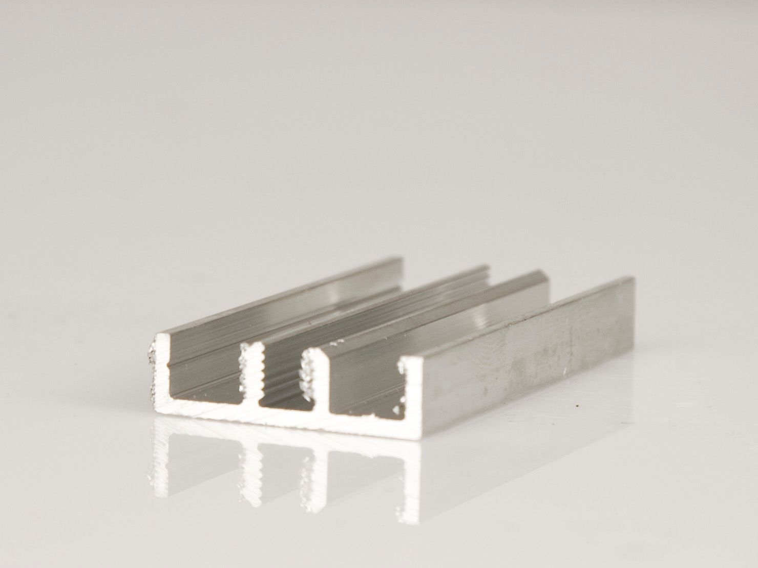 Silberner Aluminium-Kühlkörper mit drei parallelen Kühlrippen auf einer reflektierenden weißen Oberfläche.