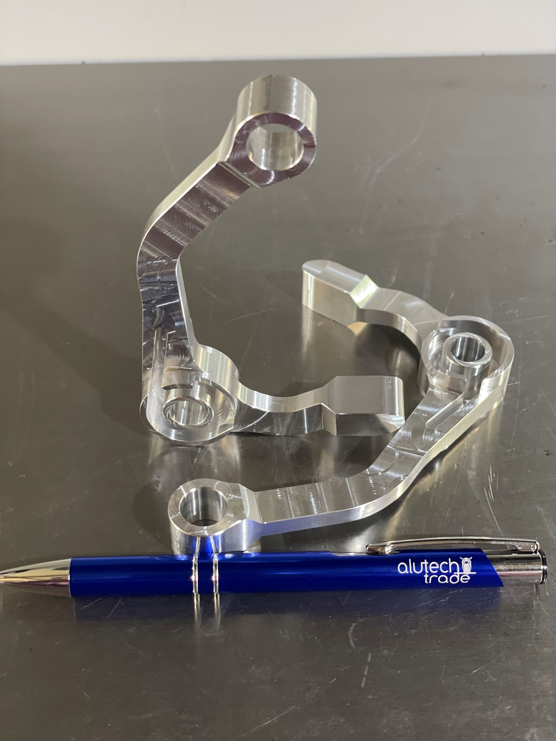 Zwei silberne, maschinell bearbeitete Metallhebel neben einem blauen Stift auf einer reflektierenden Oberfläche.