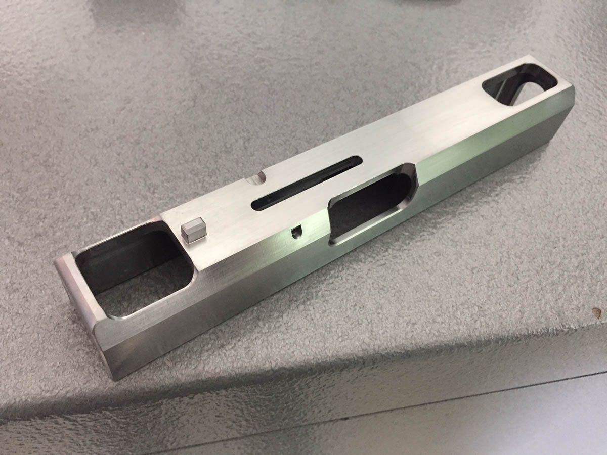 Metallener Pistolenverschluss mit mehreren Öffnungen und gefrästen Oberflächen.