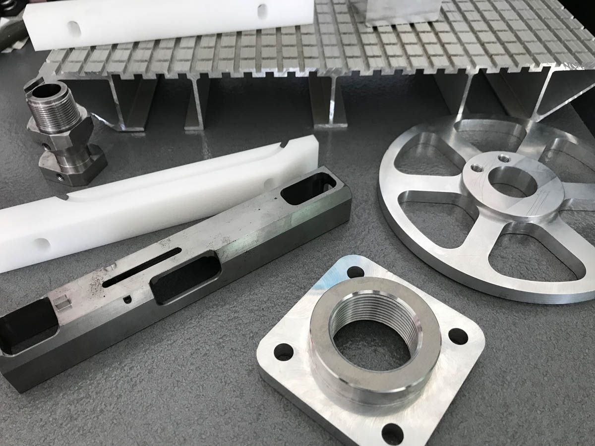 Verschiedene industrielle Metall- und Kunststoffteile, darunter ein Rad, Gewindefittings und eine Gitterplattform.