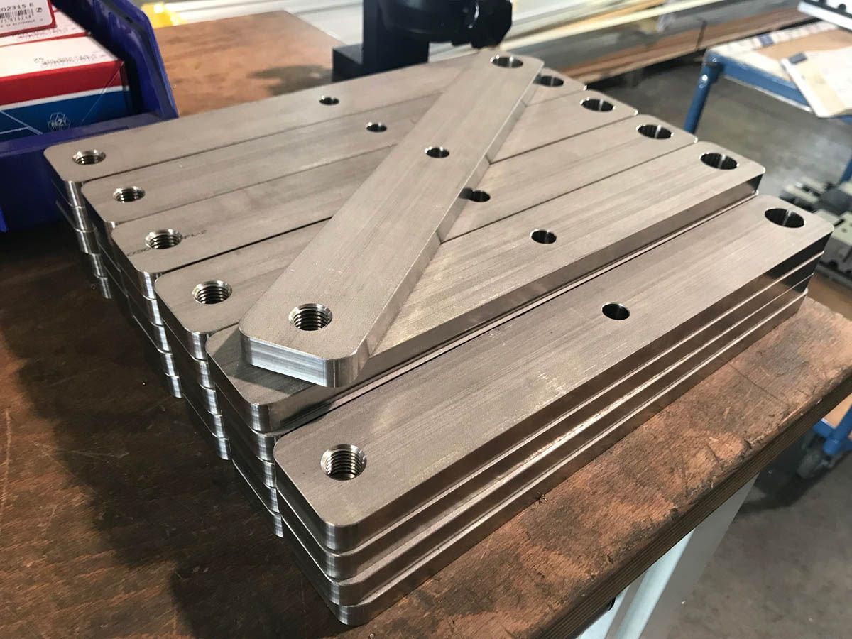 Stapel rechteckiger Metallplatten mit gebohrten Löchern auf einer Werkbank.