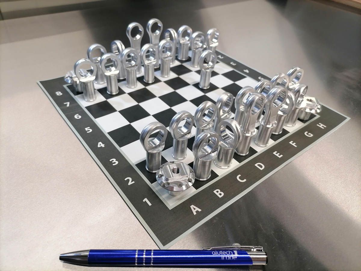 Schachspiel mit metallenen Schraubenschlüsselfiguren auf einem Schachbrett, im Vordergrund liegt ein Stift.