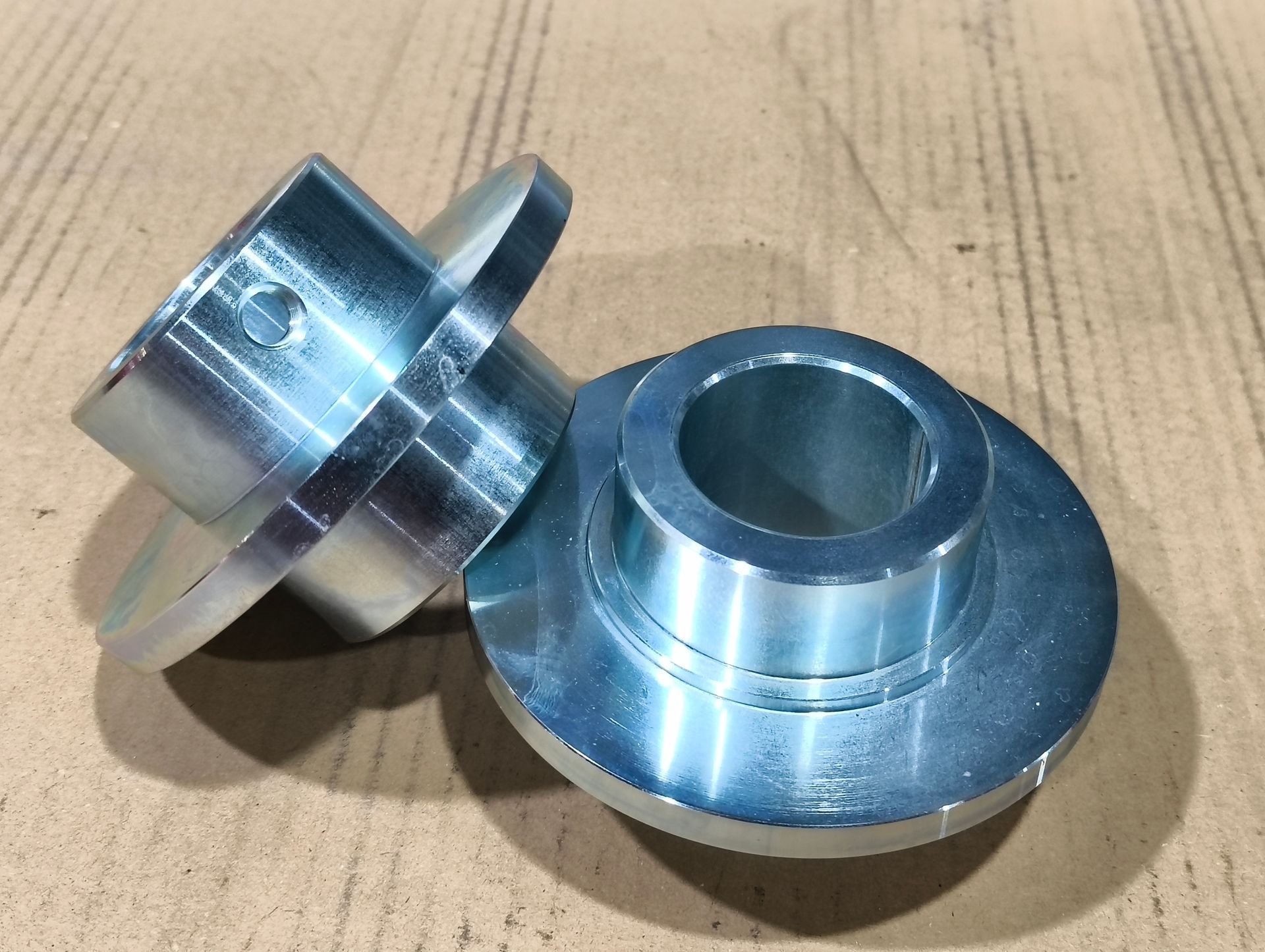 Zwei silberne Metallbuchsen mit Flanschen auf einer hellbraunen Oberfläche.
