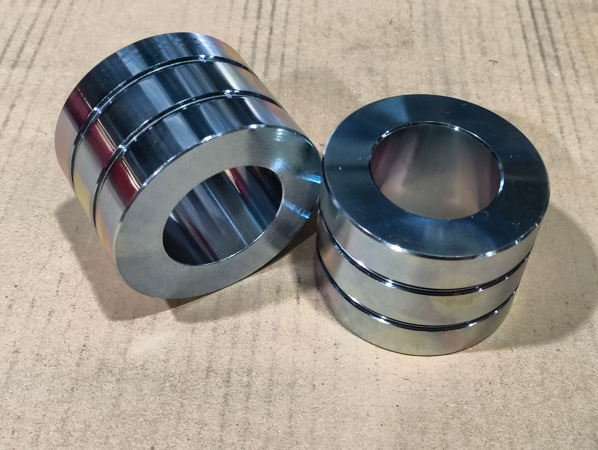 Zwei Stapel glänzender, zylindrischer Magnete auf einer hellbraunen Oberfläche. Jeder Stapel besteht aus drei Ringen.