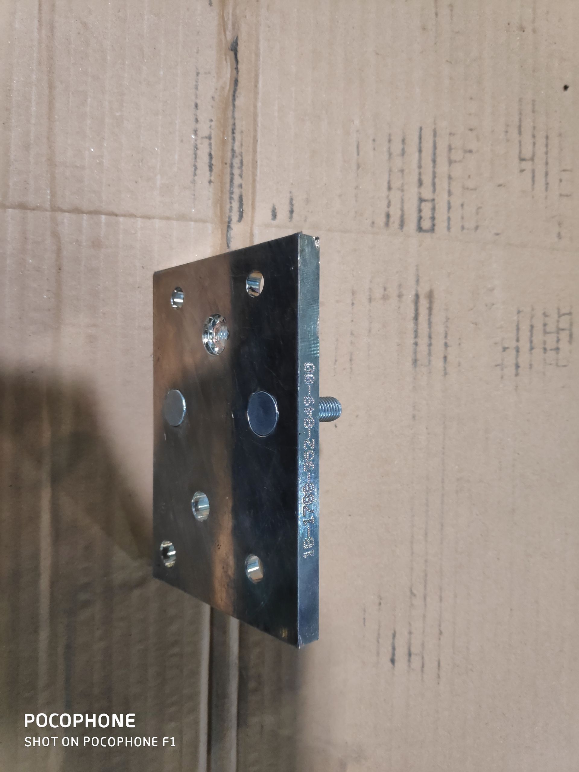 Metallplatte mit einem hervorstehenden Bolzen, auf Karton montiert. Die Platte weist mehrere Löcher auf.