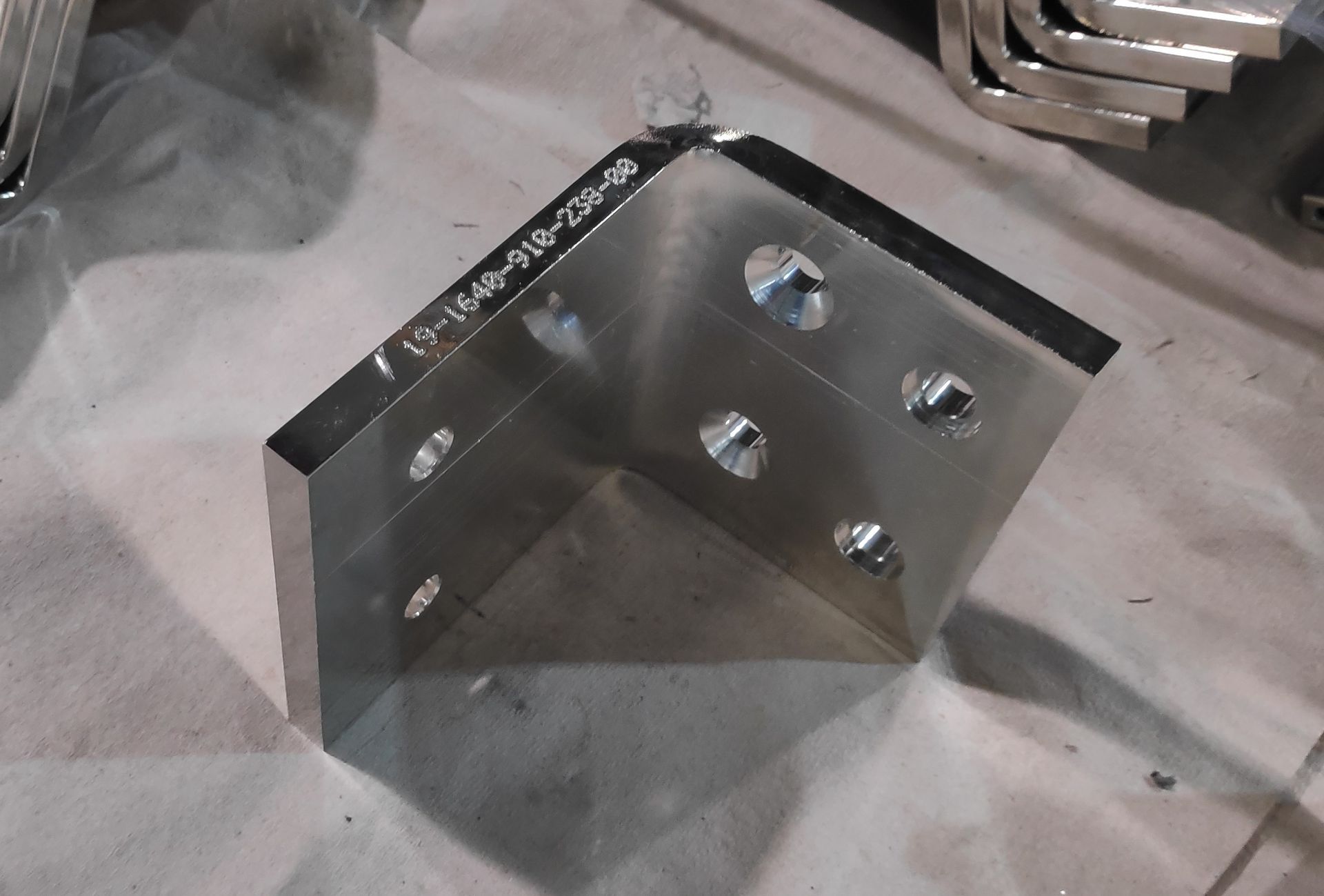 Eine rechtwinklige Metallhalterung mit mehreren Löchern, die auf einer leichten Oberfläche steht.