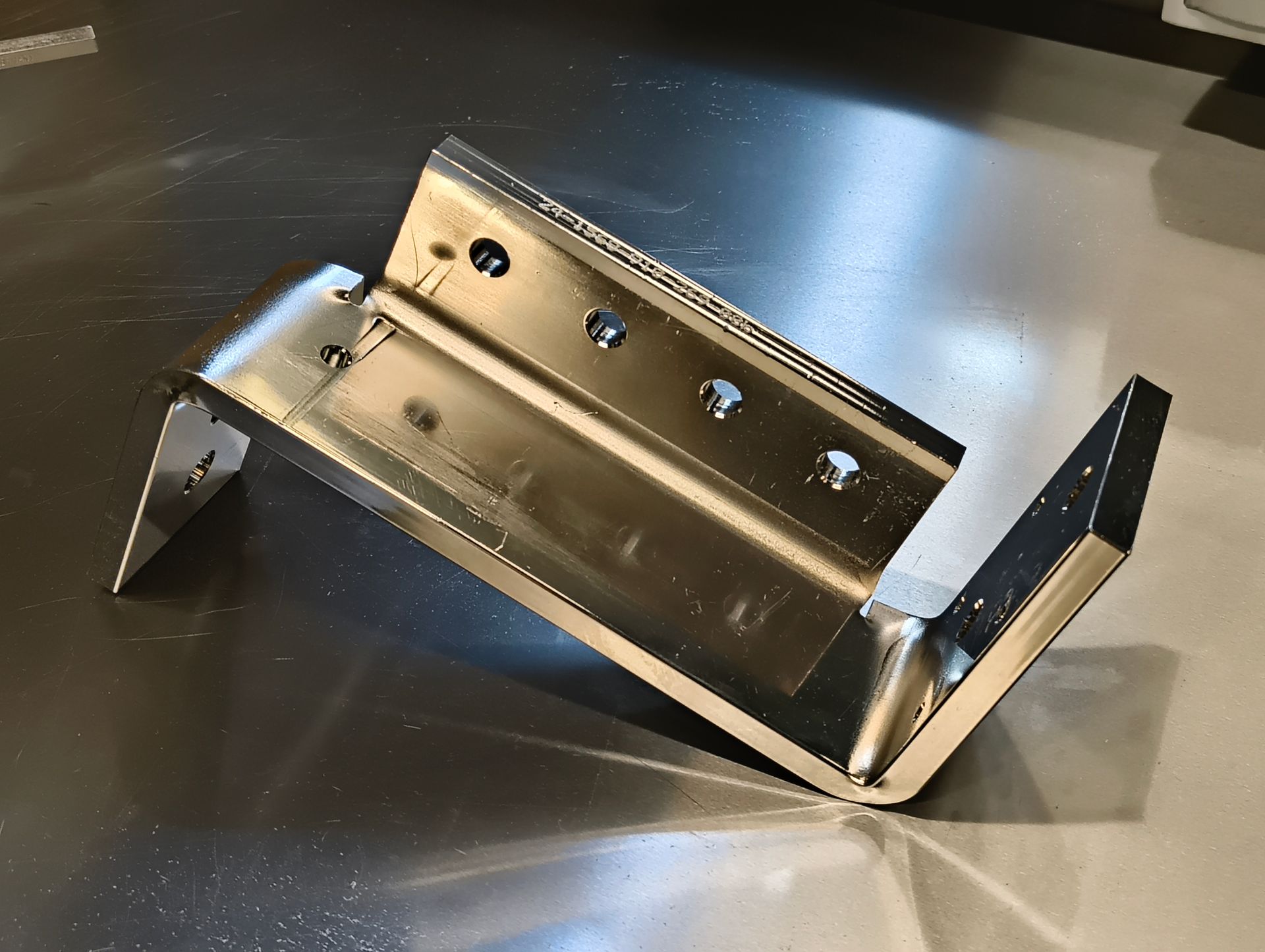 Glänzende Metallhalterung mit mehreren Löchern, die auf einer reflektierenden Oberfläche ruht.