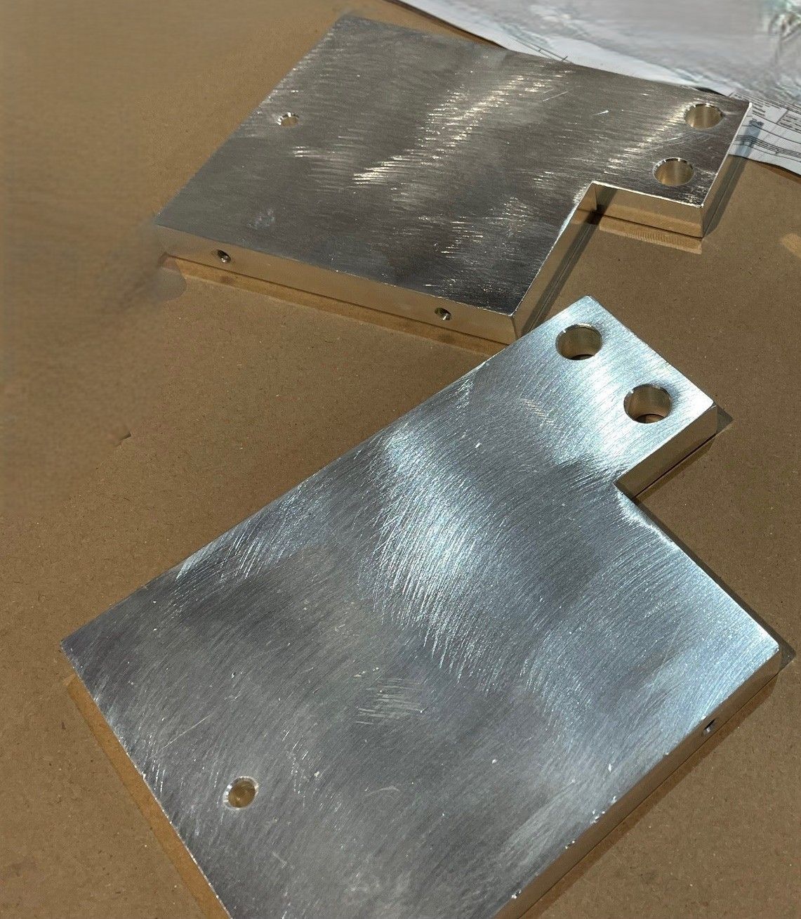 L-förmige Metallplatten, möglicherweise maschinell gefertigt, mit mehreren Löchern und einer gebürsteten Oberfläche