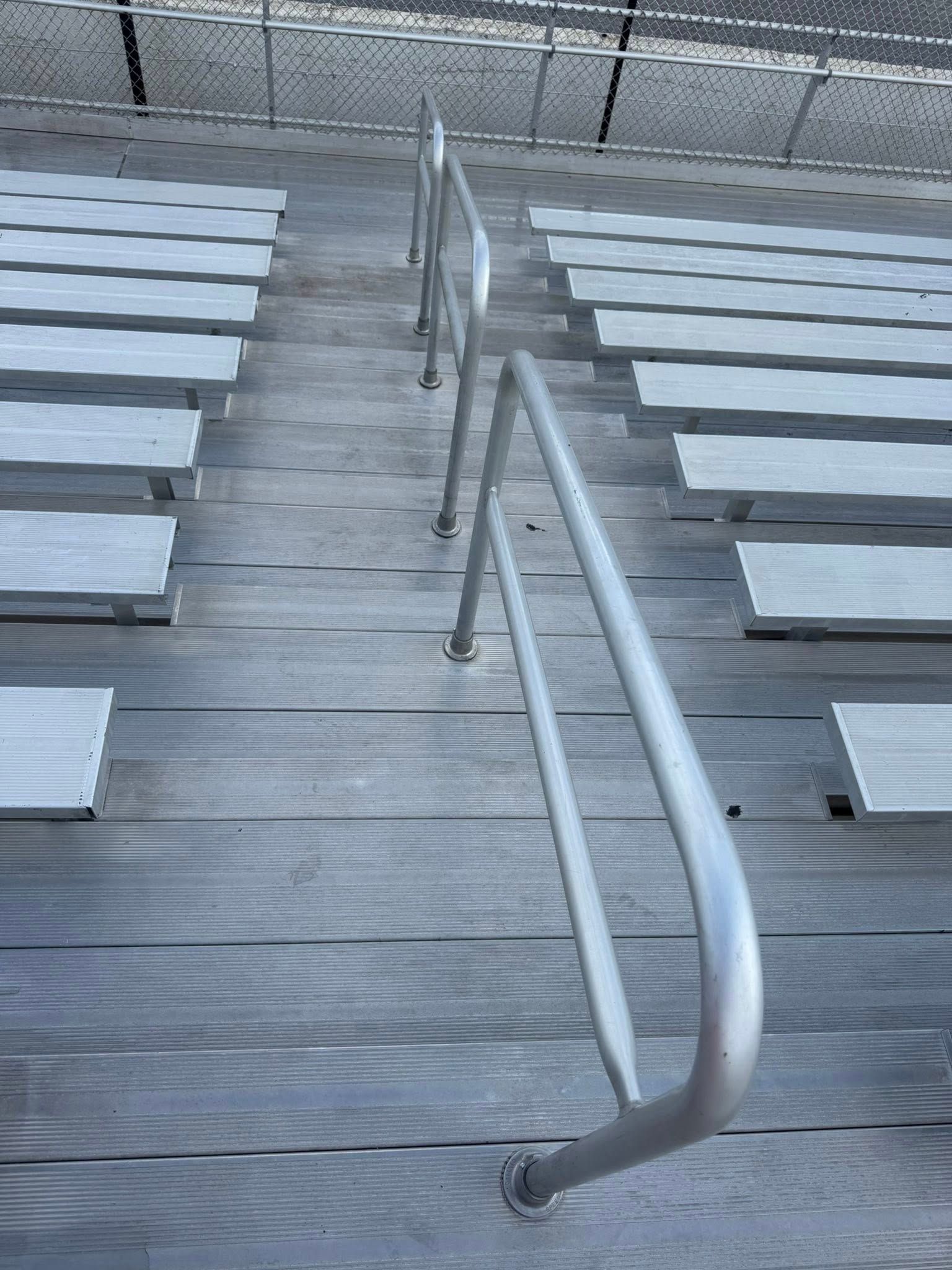 Empty silver metal bleachers with a central handrail leading up the stairs.