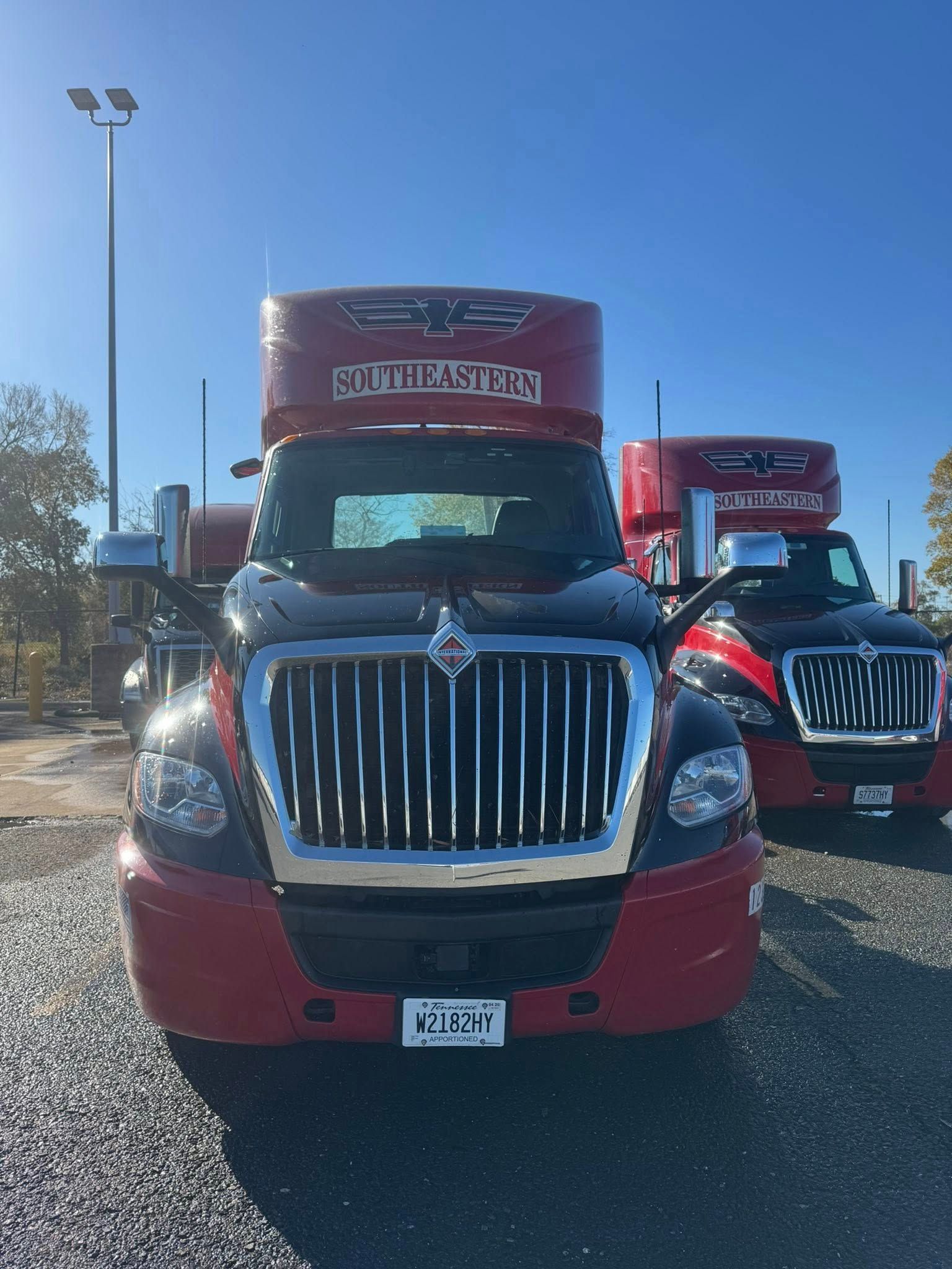 Two red and black International semi-trucks parked on a gravel lot under a clear blue sky.