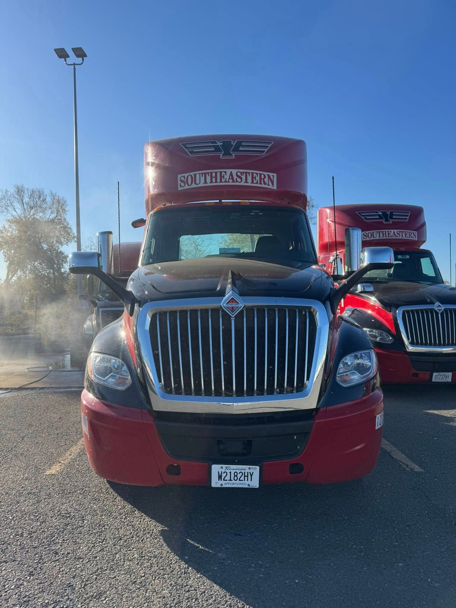 Two red and black International semi-trucks parked side-by-side on a gravel lot under a clear blue sky.
